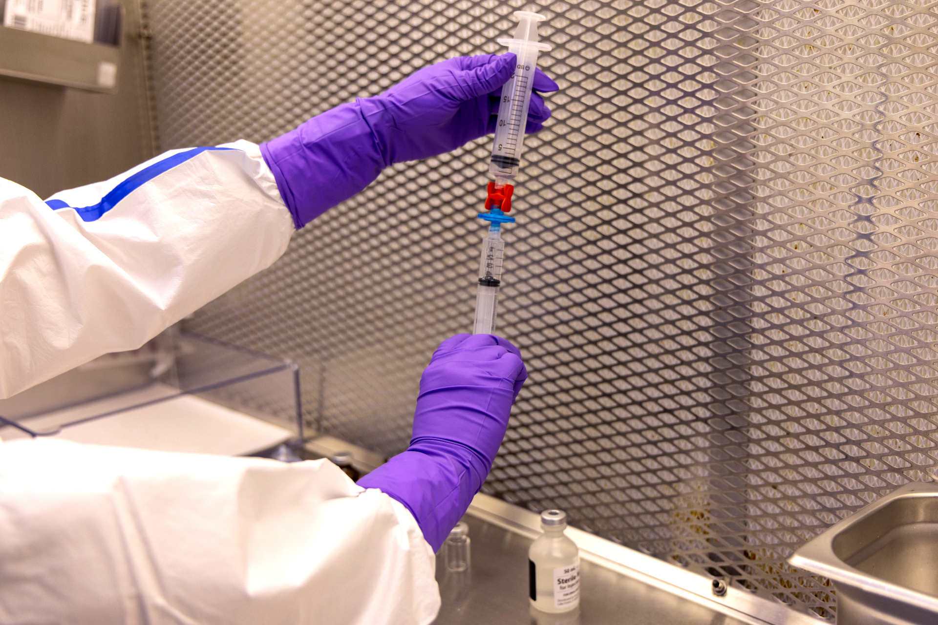 Pharmacist in purple gloves preparing sterile syringes for intravitreal injection in a cleanroom hood